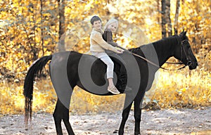 Two children boy and girl riding on horse in autumn