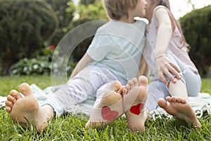 two children, a boy and a girl, are sitting on the grass, with red hearts painted on their bare feet