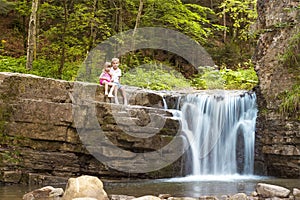 Two children boy and girl sitting near waterfall in forest