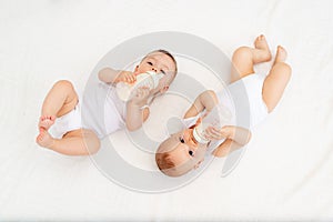 Two children a boy and a girl-twins of 8 months drink milk from a bottle on the bed in the nursery, feeding the baby, baby food