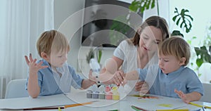 Two children of boys and mother are engaged in creative development doing homework by fingering on paper. The