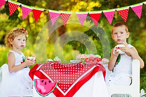 Two children brother and sister drink tea on beautiful decorated picnic. Hungry kids boy and girl eating outdoors. What to do in