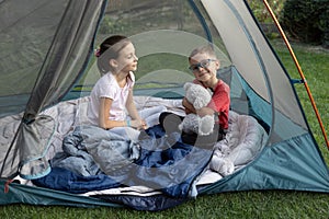 Two children, brother and sister, are sitting in a tent on a warm sunny day