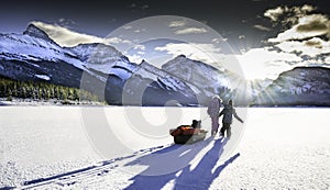 Two children drag a sled full of ice fishing gear across frozen ice and snow