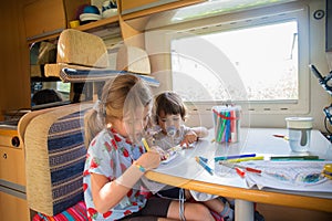 Two children drawing on a campervan during a road trip stop