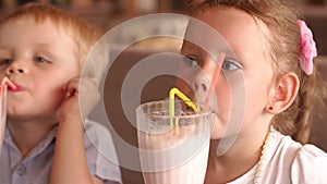 Two children drinking milkshakes in cafe outdoors.