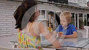 Two children eat fast food in a street cafe on the riverbank in summer.