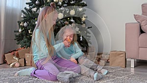 Two children girls sisters playing toys sitting near Christmas tree at home.