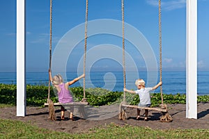 Two children have fun swinging on rope swing at beach