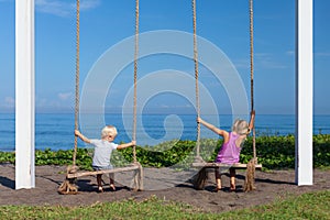 Two children have fun swinging on rope swing at beach