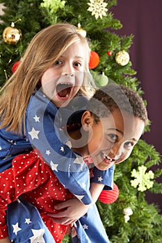 Two Children Having Fun In Front Of Christmas Tree