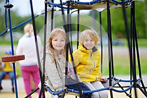 Two children having fun on playground in park. Spring/summer/autumn active sport leisure for kids. Outdoor activity for baby and