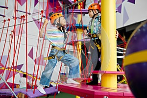 Two children in helmets climb on zip line