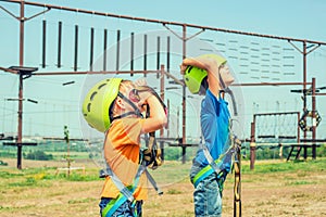 Two children in helmets and safety gear are looking up in an extreme park