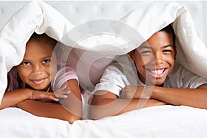 Two Children Hiding Under Duvet In Bed