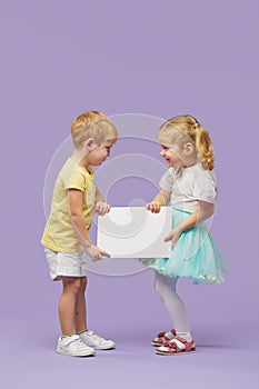Two children holding a white banner on purple background. Funny Faces. Copy space for text