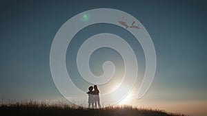 Two children launch a kite in the field at sunset.