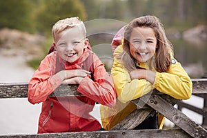 Two children leaning on a wooden fence in the countryside smiling to camera, close up