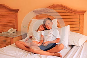 Two children lie on a bed with white sheets in a hotel room on vacation.