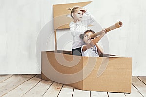 Two children little girls home in a cardboard ship play captains
