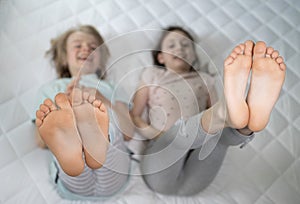 Two children lying on the bed cheerfully raised their bare feet up photo