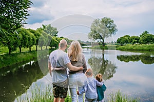 Two children, mother and father looking on lake in summer day back view