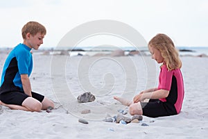 Two children in neoprene swimsuits playing on the beach with sand