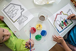 Two children painting a sketch of a family in a house