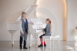 Two children play the piano and sing in a white room.