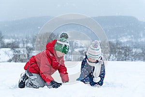 Two children play with the snow on frosty winter day. Siblings outside in the snowy day