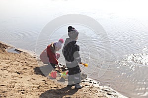 Two children are playing on the beach near the river.