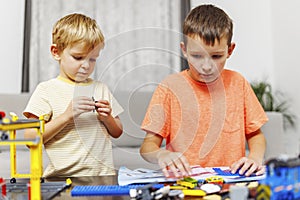 Two children playing and building with colorful plastic bricks at the table