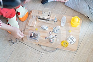 Two Children are playing with busy board toy on the wooden floor together. Childrenâ€™s educational busy board toy for developing