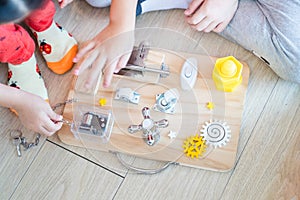 Two Children are playing with busy board toy on the wooden floor together. Childrenâ€™s educational busy board toy for developing