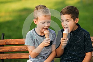 Two children are playing in the park. Two beautiful boys in T-shirts and shorts have fun smiling. They eat ice cream