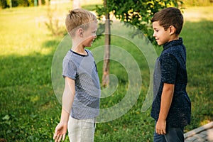 Two children are playing in the park. Two beautiful boys in T-shirts and shorts have fun smiling. They eat ice cream