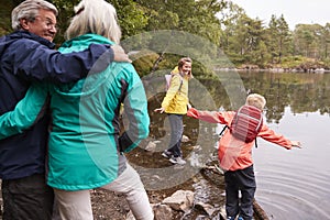 Two children playing at the shore of a lake, their grandparents in the foreground, Lake District, UK photo