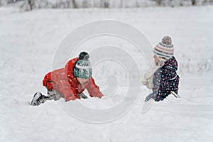 Two children are playing in the snow. Children in knitted hats and puffy jackets have fun on winter day