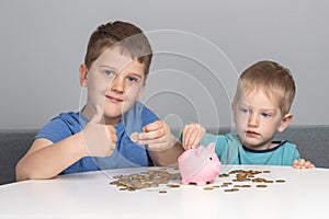 Two children put coins in piggy bank. Boys are investing in their future education. The boy smiles and shows thumbs up