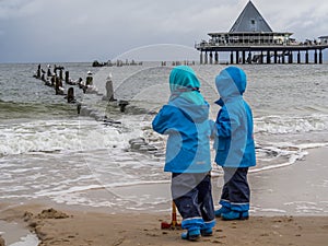 Two children in rainwear play by the sea