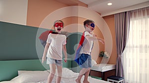 Two children in red and blue Superman costume,girl and boy superheroes, are jumping in room on bed,in children's