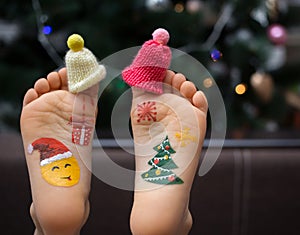 Two children`s bare feet in small caps on the toes with painted pictures on the New Year`s theme