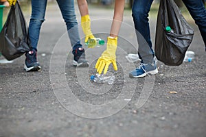 Two children`s hands in yellow latex gloves holding black garbage bags on an asphalt background. Ecology protection