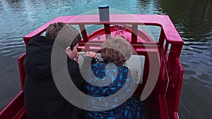Two children sail in an electric boat on a lake during the school holidays