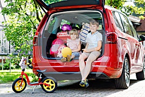 Two children, school boy and preschool girl sitting in car trunk before leaving for summer vacation with parents. Happy