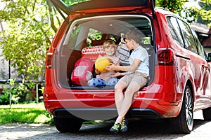Two children, school boy and preschool girl sitting in car trunk before leaving for summer vacation with parents. Happy