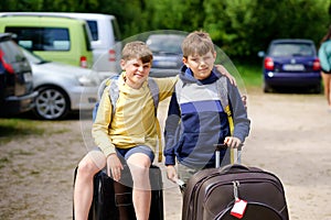 Two children, school boys sitting on suitcases before leaving for summer vacation camp. Happy kids, siblings, twins