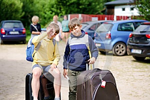 Two children, school boys sitting on suitcases before leaving for summer vacation camp. Happy kids, siblings, twins