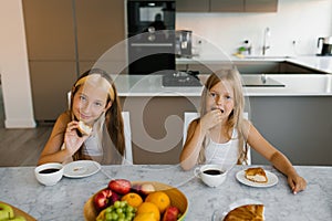 Two children sisters have breakfast in the morning at the table in the kitchen