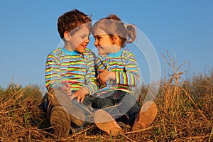 Two children sit on dry grass